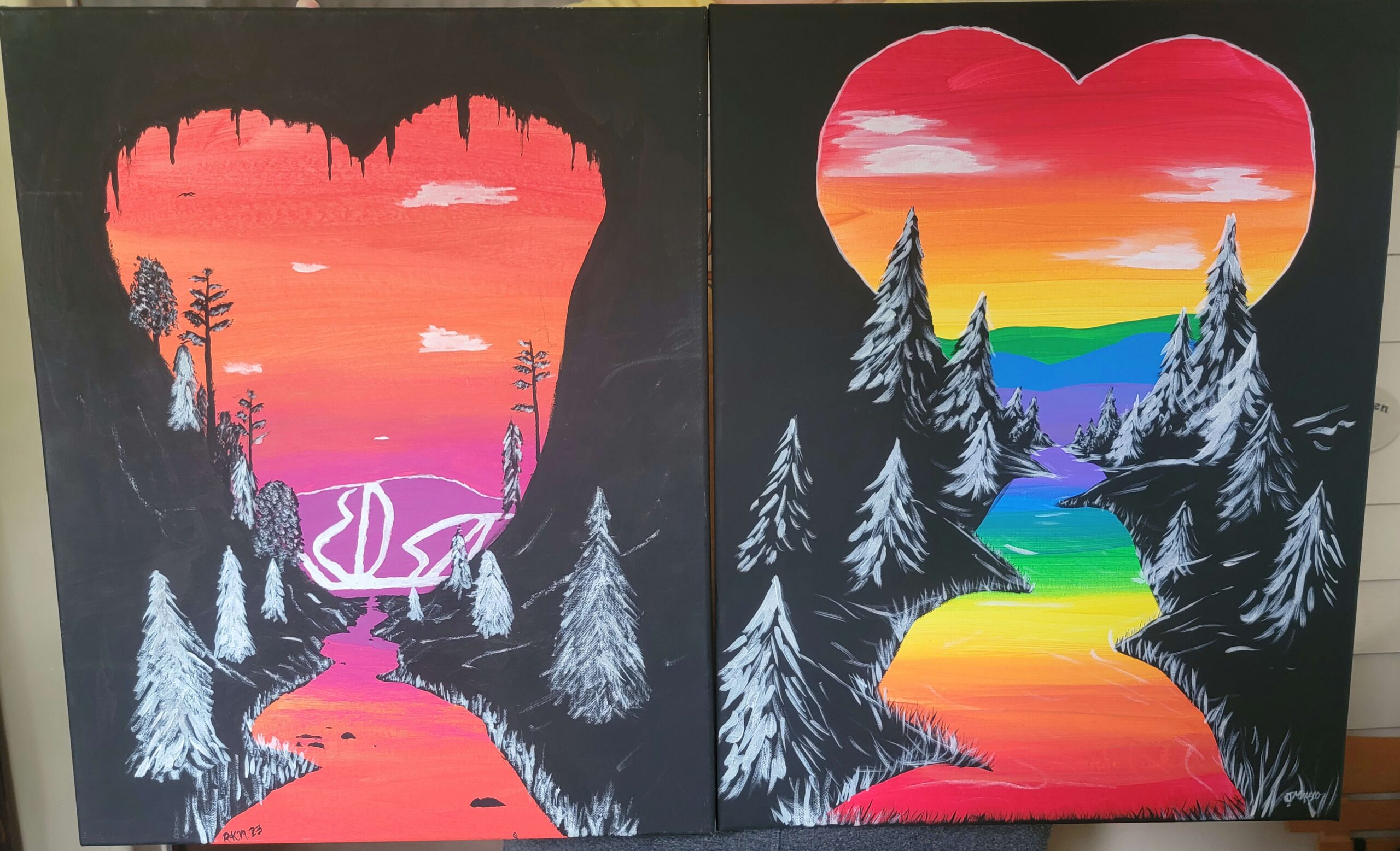 Two paintings side by side, from Pride Paint Night. Both paintings feature a black background that cuts an image with color. The color creates a heart in the sky and a river below reflecting the colors of the sky. White trees are painted to the left and right of the river. The left hand painting has the lesbian flag colors in the sky. The painting on the right has a rainbow sky.